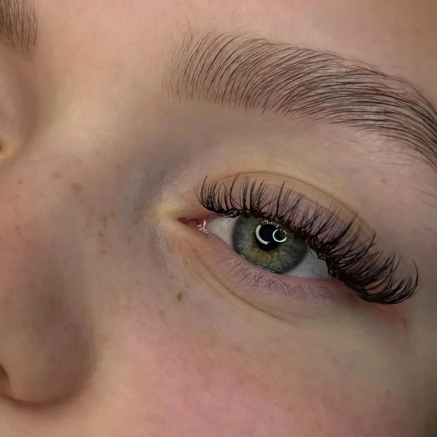 Lähikuva asiakkaan silmästä, jossa on ripsipidennykset ja huolitellut kulmat.